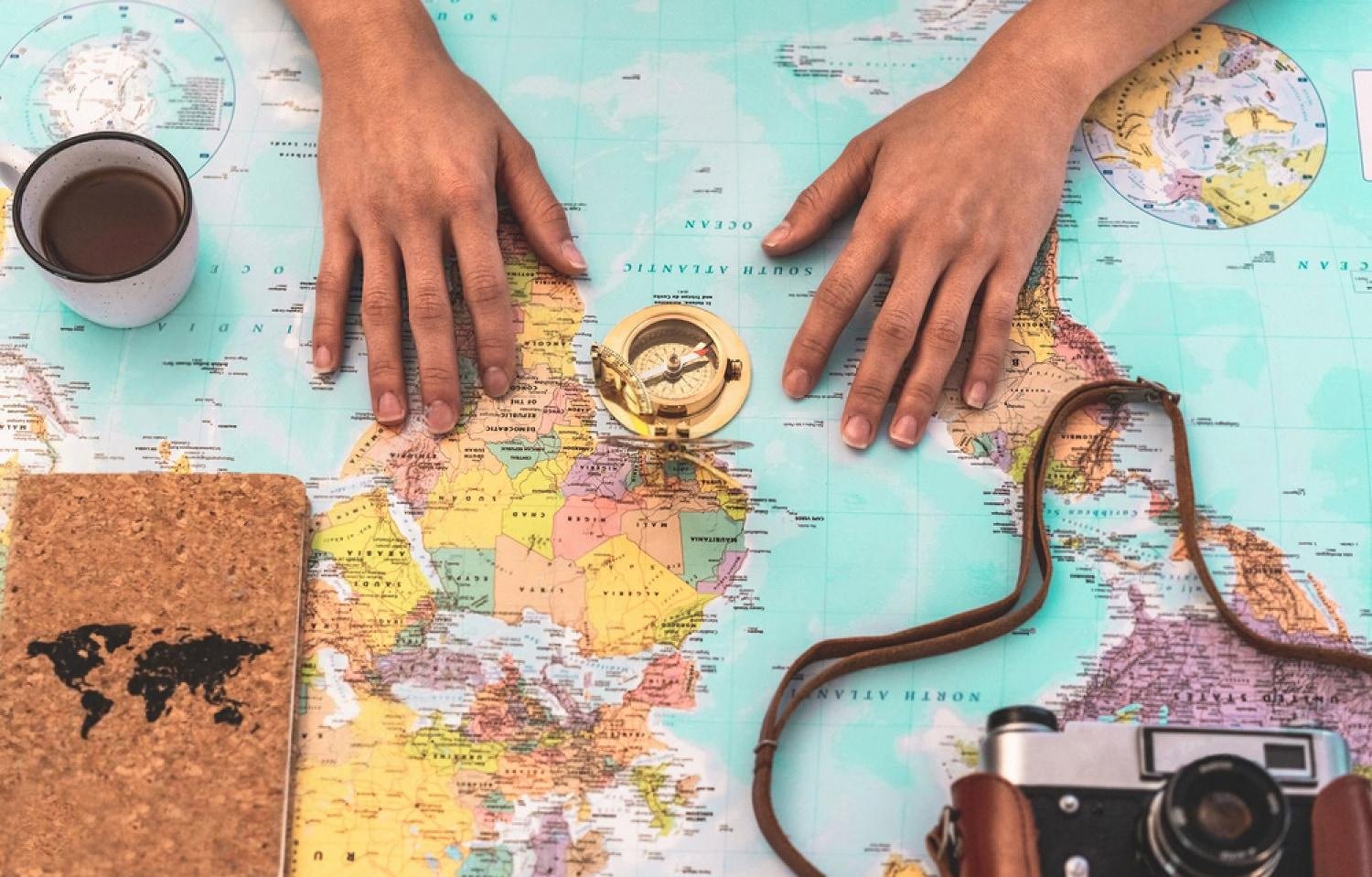 Hands on a world map planning an Australia road trip with compass and camera